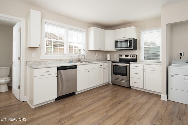 kitchen featuring appliances with stainless steel finishes, sink, light hardwood / wood-style flooring, white cabinets, and washer / clothes dryer