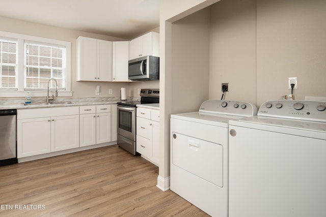 kitchen with appliances with stainless steel finishes, washing machine and dryer, white cabinets, a sink, and light wood-type flooring