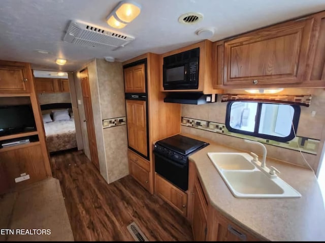 kitchen with black microwave, a sink, visible vents, brown cabinetry, and dark wood finished floors