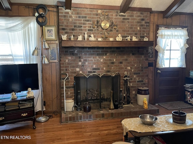 living room featuring hardwood / wood-style flooring, wooden walls, a textured ceiling, a brick fireplace, and beamed ceiling