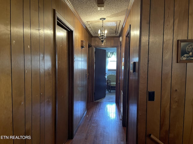 hall featuring wood walls, dark hardwood / wood-style flooring, a chandelier, crown molding, and a textured ceiling