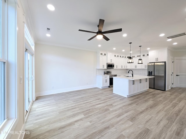 kitchen with stainless steel appliances, a kitchen island with sink, pendant lighting, and white cabinets