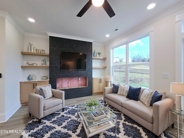 living room featuring crown molding, a fireplace, light hardwood / wood-style floors, and ceiling fan