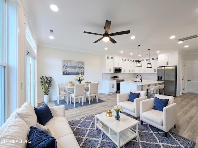 living room featuring crown molding, sink, ceiling fan, and light hardwood / wood-style flooring