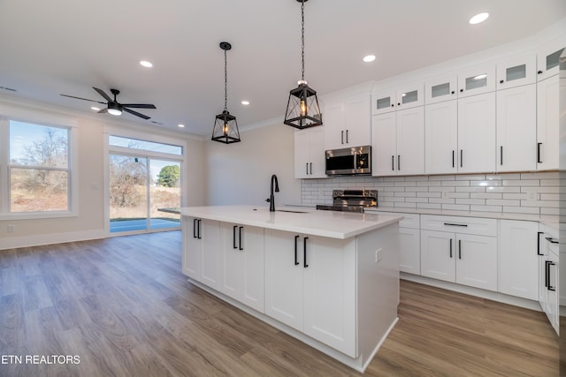 kitchen with sink, white cabinetry, crown molding, appliances with stainless steel finishes, and a kitchen island with sink