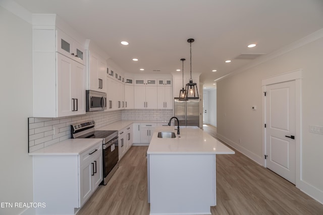 kitchen with sink, hanging light fixtures, appliances with stainless steel finishes, a kitchen island with sink, and white cabinets