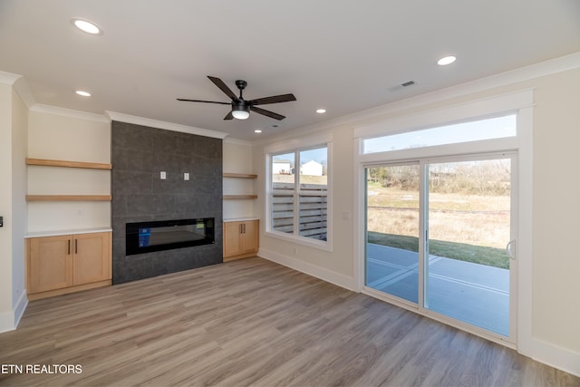 unfurnished living room featuring built in features, a fireplace, ornamental molding, ceiling fan, and light hardwood / wood-style flooring