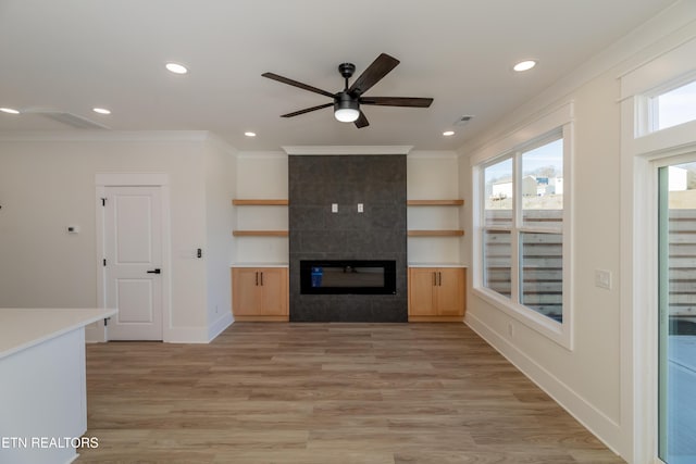 unfurnished living room featuring crown molding, ceiling fan, a fireplace, and light hardwood / wood-style floors