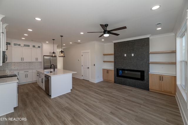 kitchen featuring white cabinetry, an island with sink, pendant lighting, stainless steel appliances, and a tiled fireplace