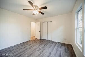 unfurnished bedroom featuring multiple windows, wood-type flooring, a closet, and ceiling fan