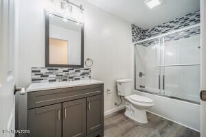 full bathroom featuring hardwood / wood-style floors, vanity, shower / bath combination with glass door, decorative backsplash, and toilet