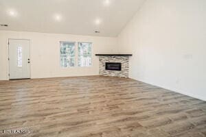 unfurnished living room with wood-type flooring, a stone fireplace, and lofted ceiling