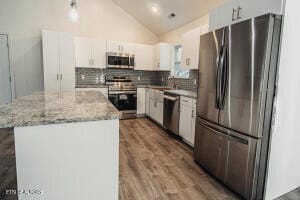 kitchen with lofted ceiling, white cabinets, a kitchen island, light stone counters, and stainless steel appliances