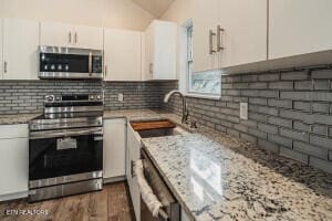 kitchen featuring white cabinets, appliances with stainless steel finishes, light stone counters, and sink