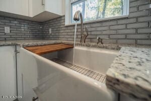 interior details with white cabinets, light stone counters, and backsplash