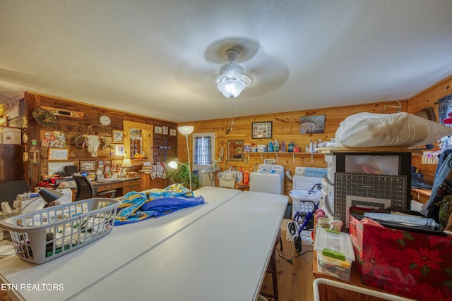 dining room with ceiling fan, wood walls, a textured ceiling, and a tile fireplace