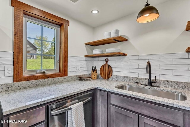 kitchen with decorative backsplash, light stone counters, stainless steel dishwasher, sink, and pendant lighting