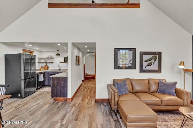 living room featuring high vaulted ceiling, light hardwood / wood-style flooring, and sink