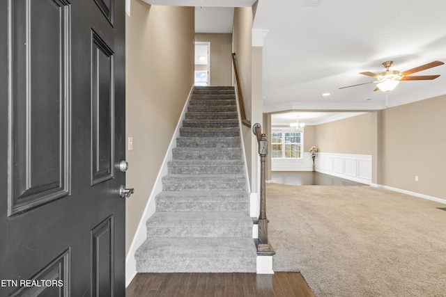 stairway with ornamental molding, ceiling fan with notable chandelier, and carpet