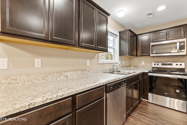 kitchen featuring sink, stainless steel appliances, dark hardwood / wood-style floors, dark brown cabinetry, and light stone counters