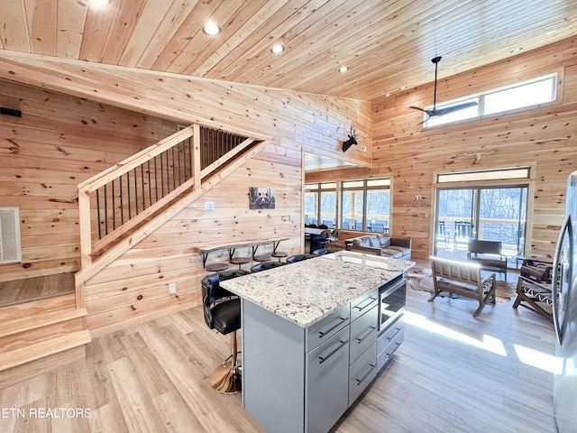 kitchen featuring a kitchen island, open floor plan, hanging light fixtures, gray cabinetry, and wood walls