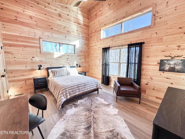 bedroom featuring light wood-style floors, wooden walls, and a high ceiling