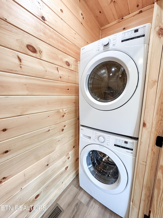 clothes washing area featuring laundry area, light wood finished floors, stacked washer and clothes dryer, and wooden walls