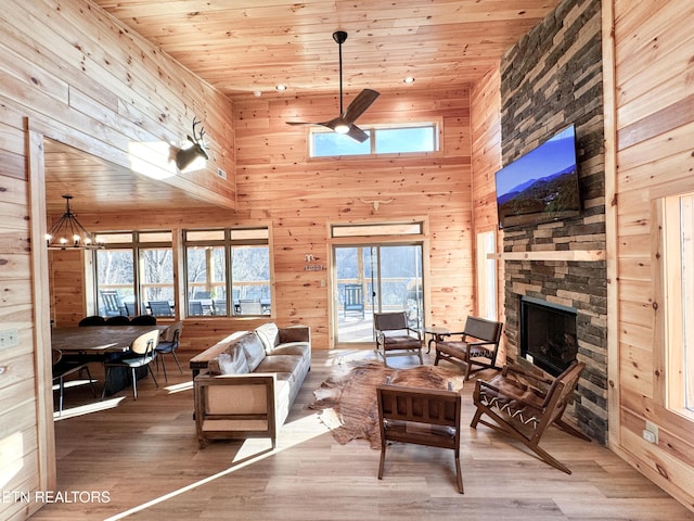 living area with wood ceiling, wooden walls, a stone fireplace, wood finished floors, and ceiling fan with notable chandelier