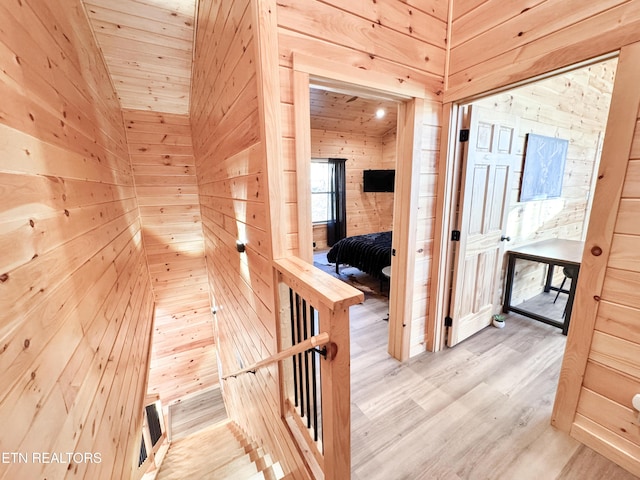 hallway with light wood-style floors, vaulted ceiling, and wooden walls