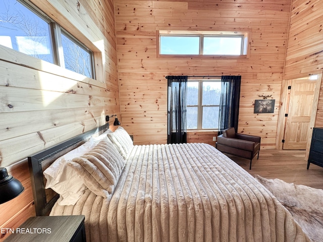 bedroom with multiple windows, a towering ceiling, light wood-style flooring, and wooden walls