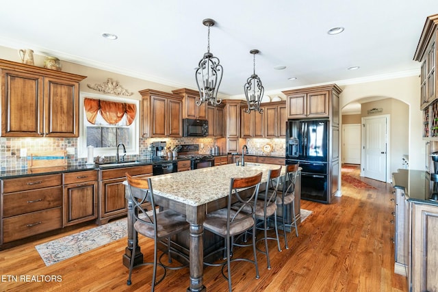 kitchen with a breakfast bar area, hanging light fixtures, black appliances, an island with sink, and dark stone counters