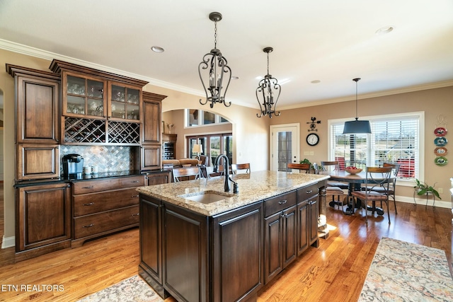 kitchen featuring decorative light fixtures, sink, light stone counters, dark brown cabinets, and light wood-type flooring