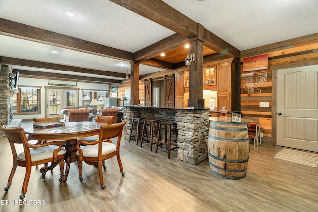 dining area featuring french doors, beam ceiling, light hardwood / wood-style flooring, wooden walls, and a barn door