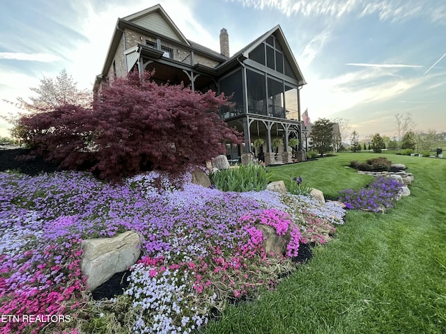 property exterior at dusk featuring a yard and a sunroom