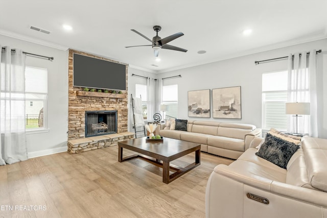 living room with light hardwood / wood-style floors, a stone fireplace, a wealth of natural light, and ceiling fan