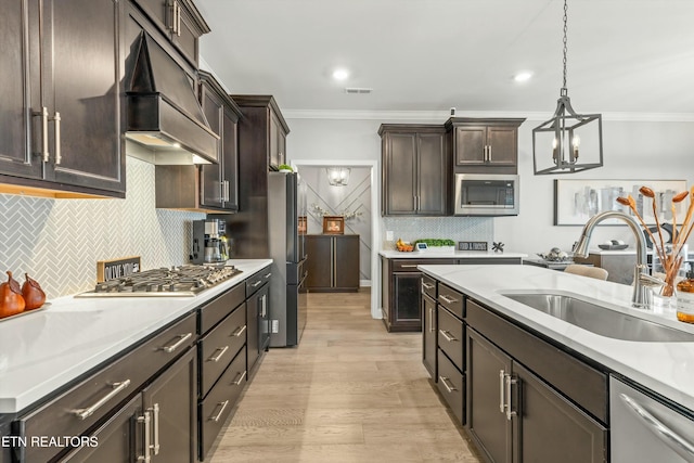 kitchen with ornamental molding, custom exhaust hood, stainless steel appliances, sink, and hanging light fixtures