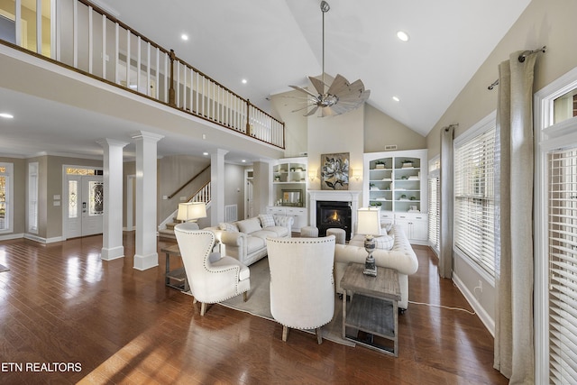 living room featuring ceiling fan, dark wood-type flooring, high vaulted ceiling, decorative columns, and crown molding