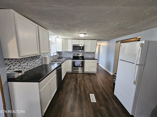 kitchen with sink, dark hardwood / wood-style floors, backsplash, white cabinets, and appliances with stainless steel finishes