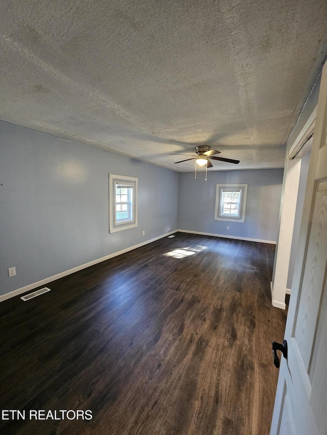 empty room with ceiling fan, plenty of natural light, dark wood-type flooring, and a textured ceiling