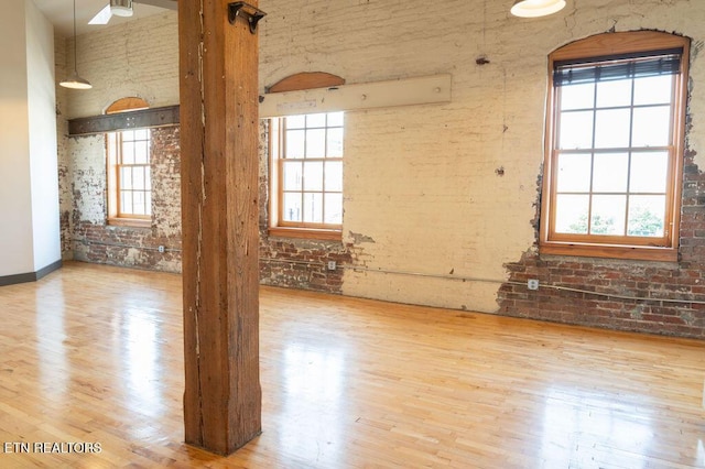 empty room featuring plenty of natural light, wood-type flooring, and brick wall