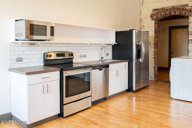 kitchen featuring appliances with stainless steel finishes, tasteful backsplash, sink, white cabinets, and washer / dryer