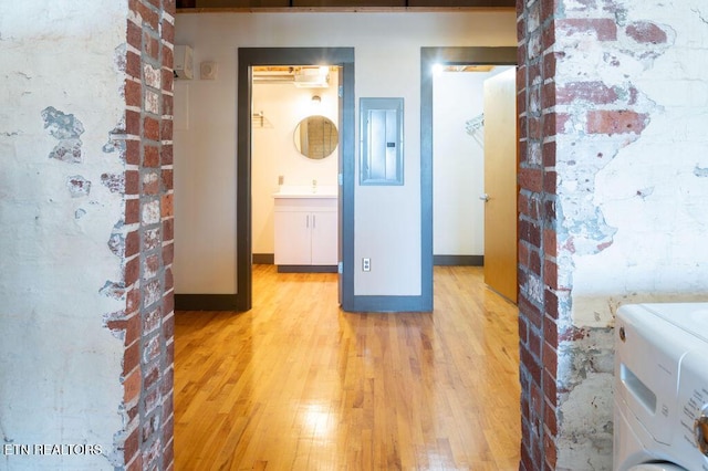 hallway with electric panel, brick wall, and light wood-type flooring