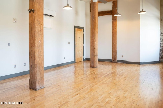 empty room with ornate columns, light wood-type flooring, a towering ceiling, and a wall mounted AC