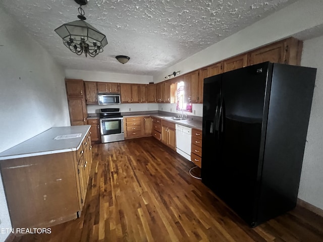 kitchen with a textured ceiling, stainless steel appliances, dark wood-type flooring, a notable chandelier, and hanging light fixtures