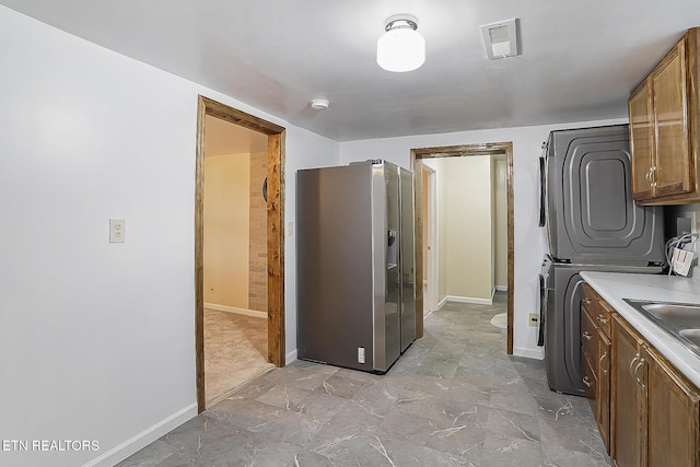 kitchen featuring stainless steel refrigerator with ice dispenser and stacked washer and clothes dryer