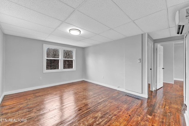 empty room featuring a wall unit AC, a drop ceiling, and dark wood-type flooring