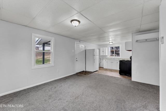 unfurnished living room featuring an AC wall unit, a drop ceiling, and carpet floors