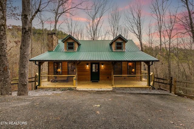 rustic home featuring covered porch, fence, driveway, and metal roof