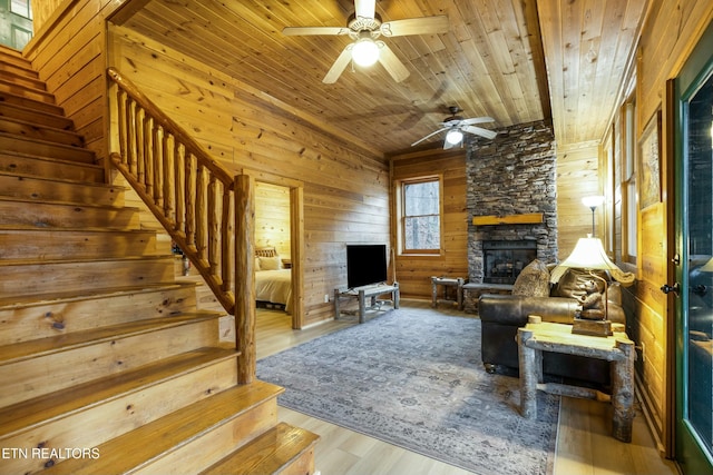 living room with wood walls, ceiling fan, a fireplace, wood-type flooring, and wood ceiling