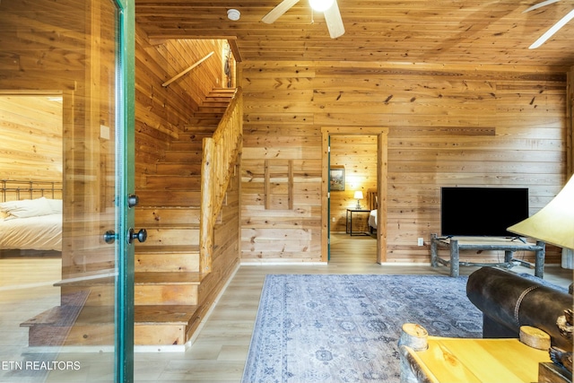 living room with hardwood / wood-style floors, ceiling fan, and wood walls